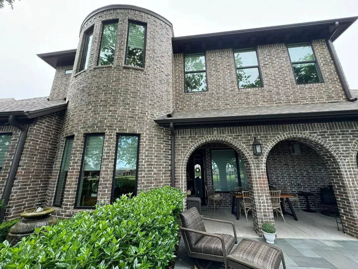Brick house with a tower and an arched porch behind greenery