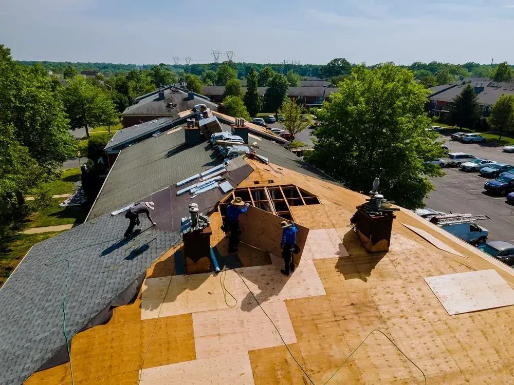 Roofing crew tearing off old shingles and replacing decking on a large multi-unit roof