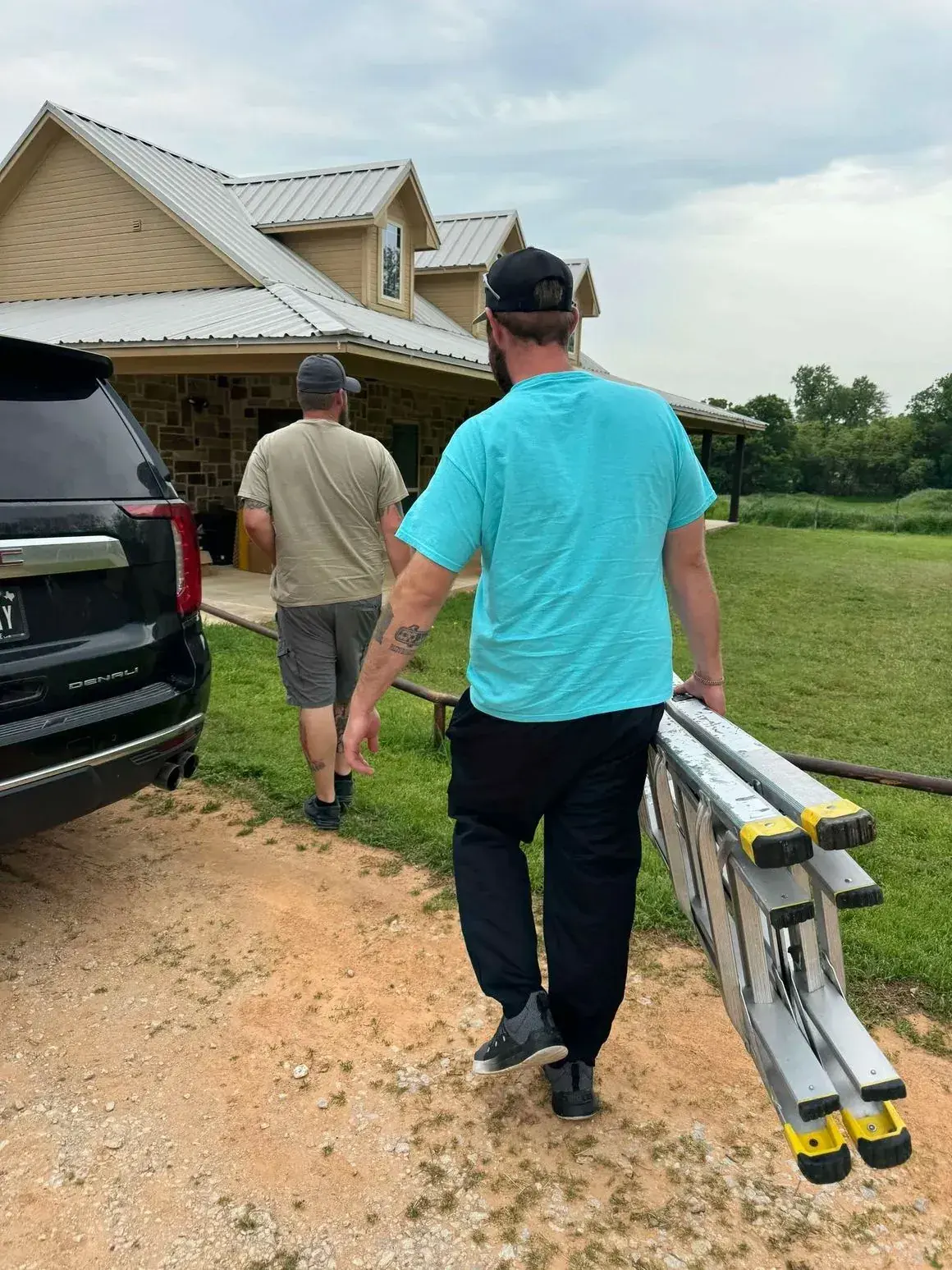 Two men walking toward a house, one carrying a folded ladder