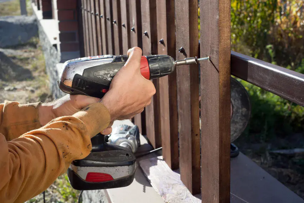 Worker driving screws into a wood fence rail with a cordless drill