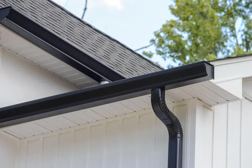 Black seamless gutter and downspout along the eave of a white board-and-batten home