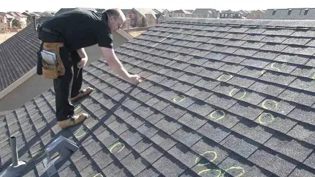 Roof inspector marking hail hits with chalk on gray asphalt shingles