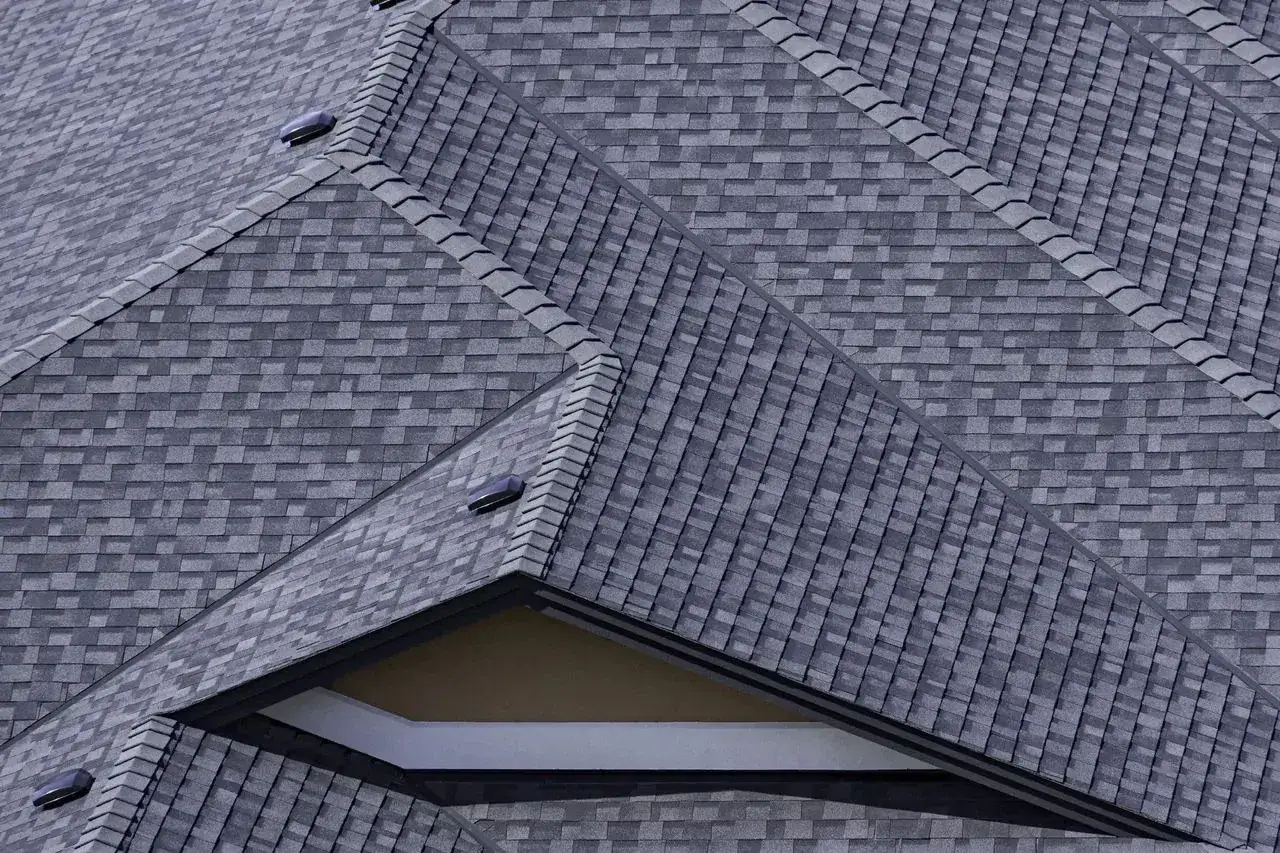 Newly installed gray architectural shingles along a roof ridge and gable