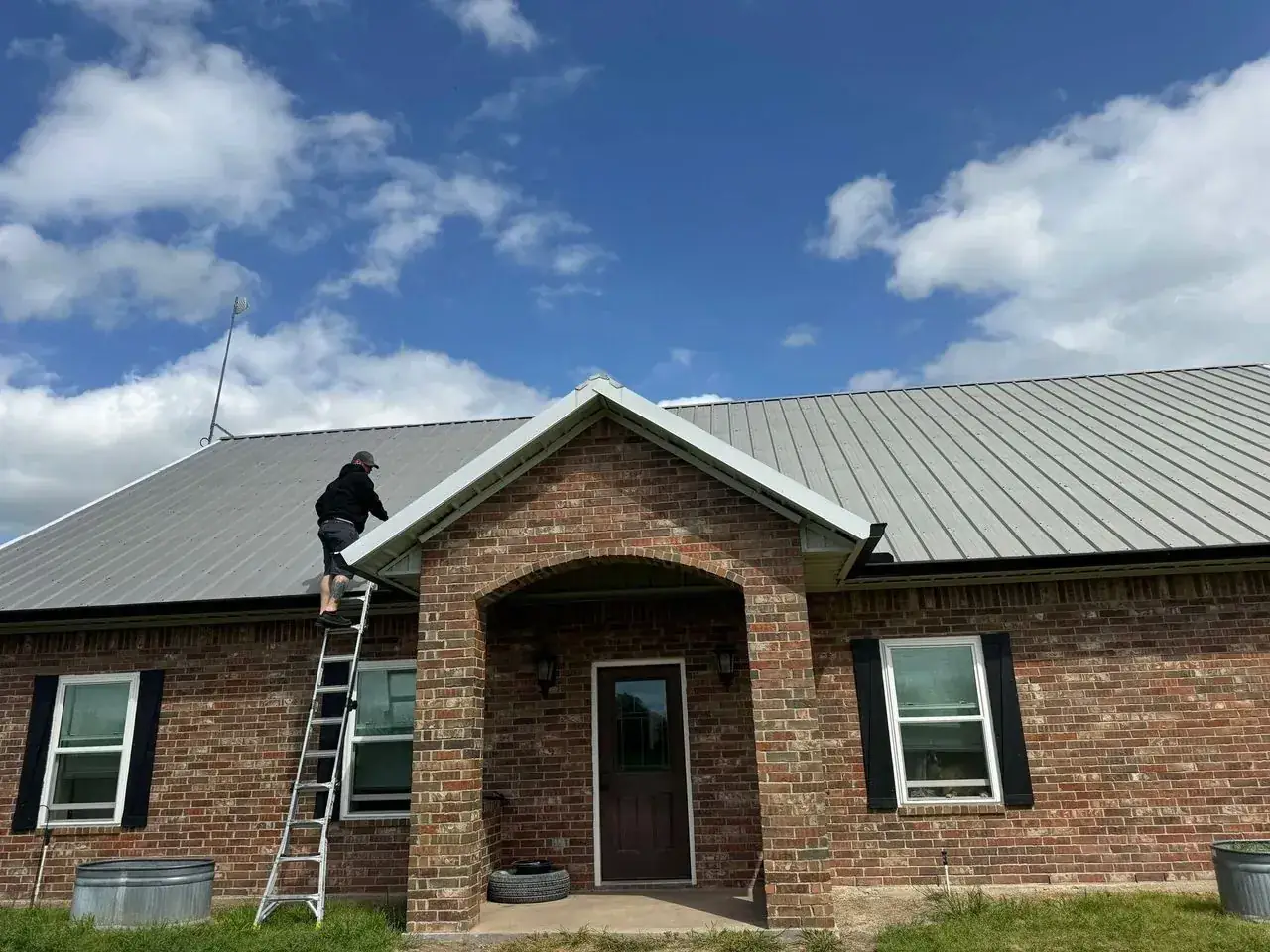 Roofer on a ladder working on the roof of a red brick house under a blue sky