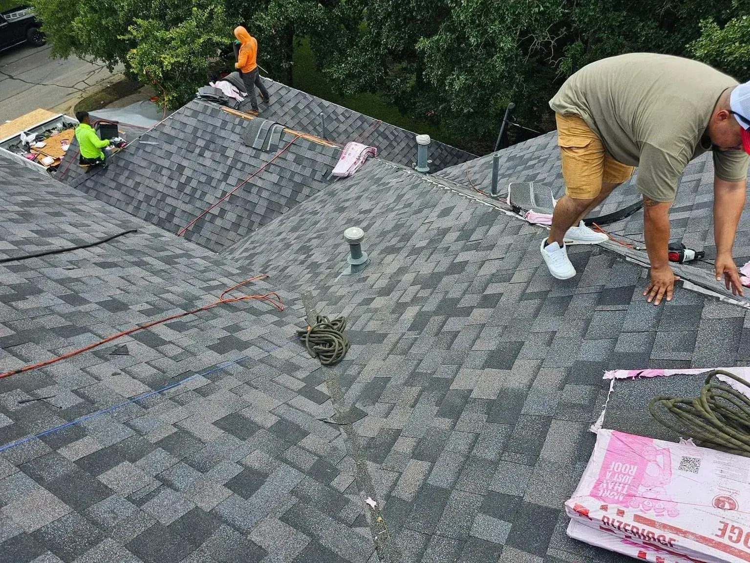 Roofers installing asphalt shingles on a multi-sloped roof.