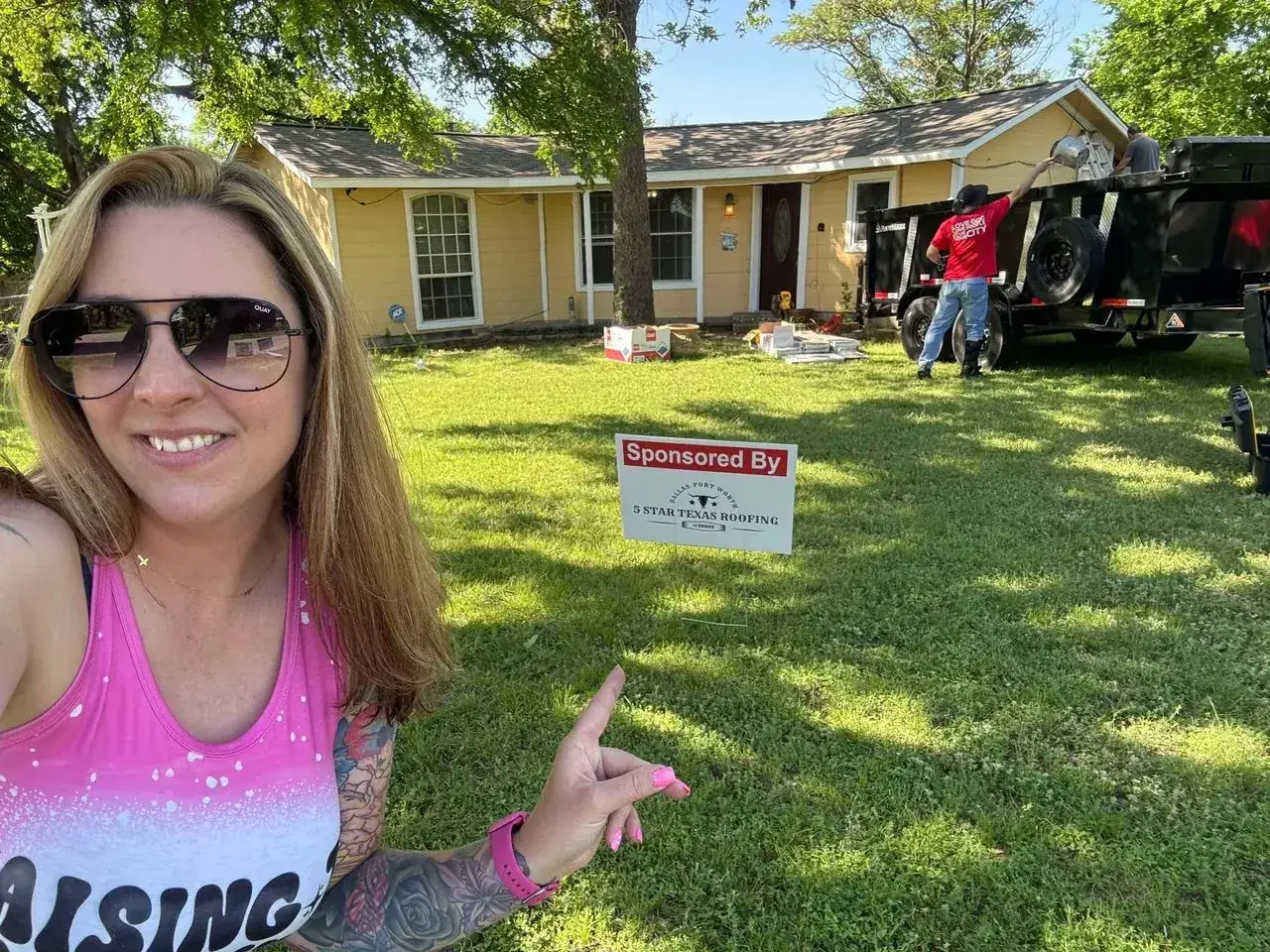 Woman pointing to a Sponsored By yard sign at a yellow house roofing job