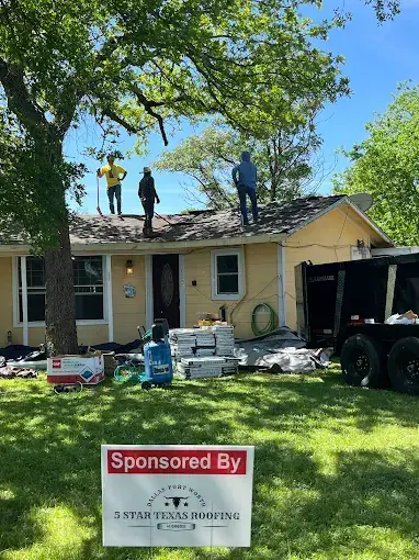 Roofing crew on a yellow house, materials and a trailer in the yard; sign reads "Sponsored By 5 Star Texas Roofing".