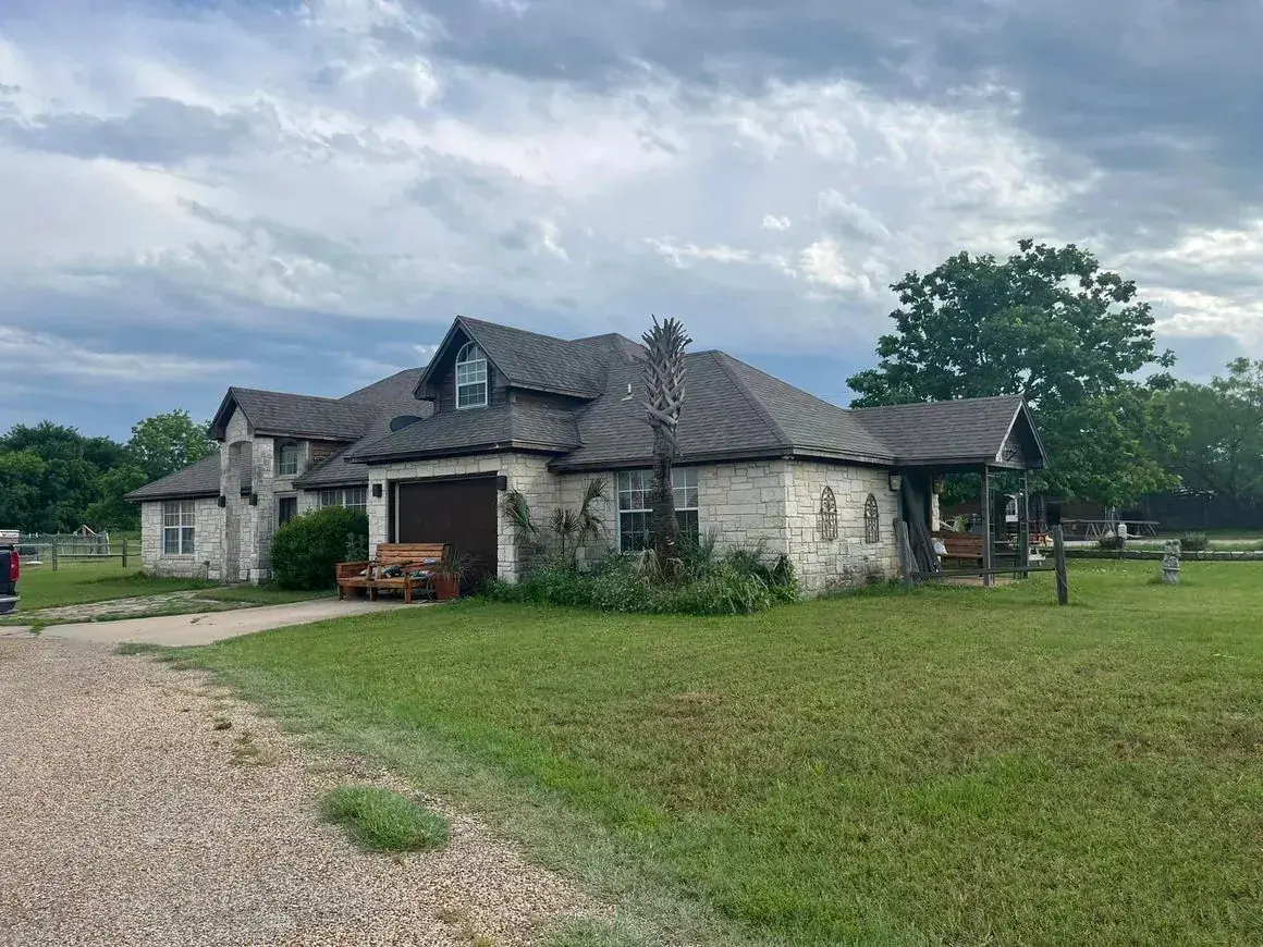 Stone house with multiple rooflines on a grassy lot under a cloudy sky