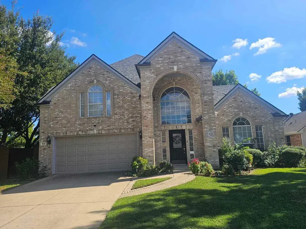 Tan brick house with an arched doorway and garage on a sunny day